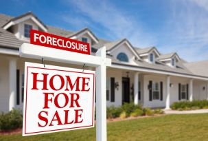 For sale sign outside a home with a "foreclosure" sign